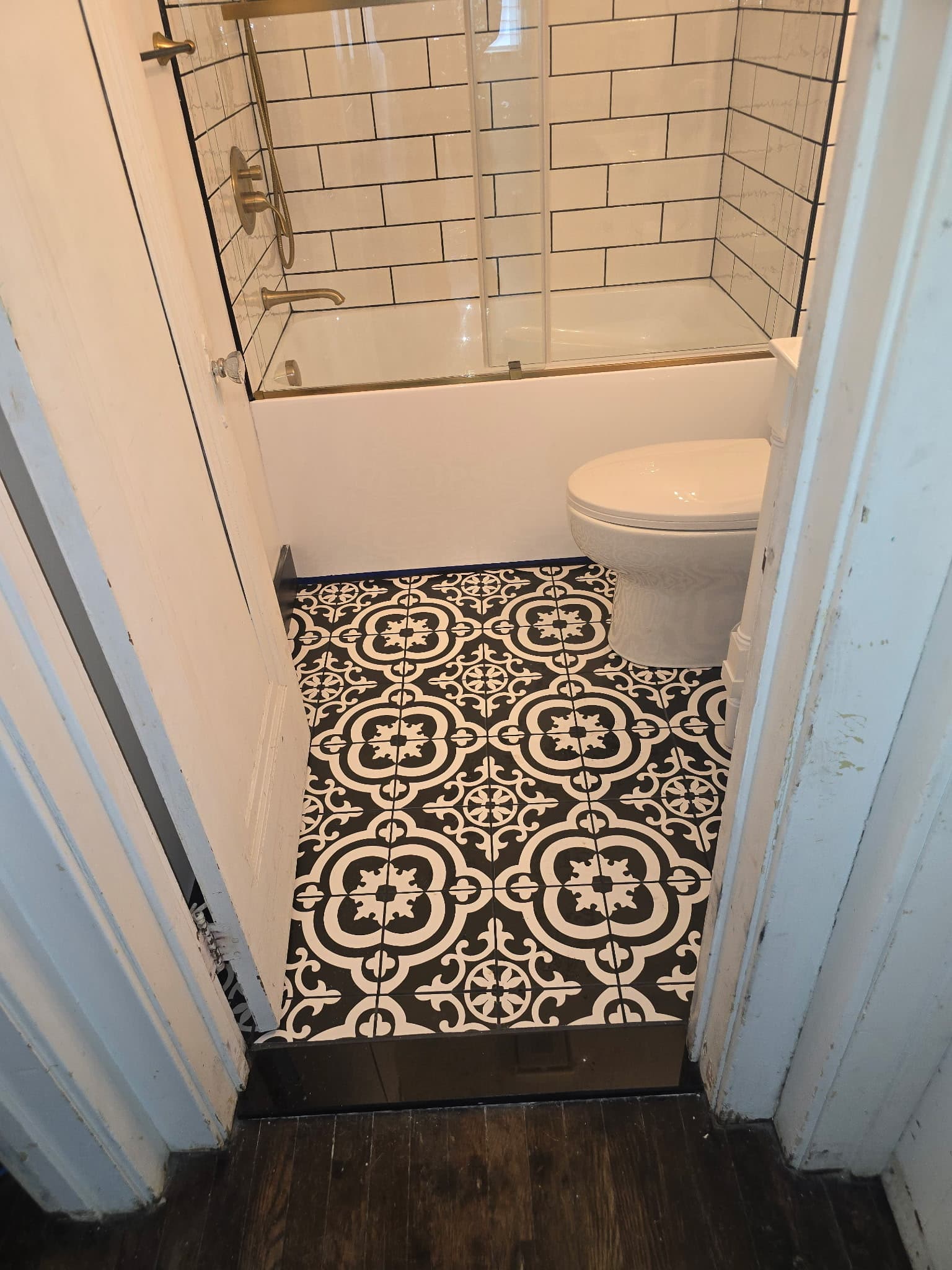 Custom bathroom with black-and-white encaustic patterned floor tile and brass shower fixtures