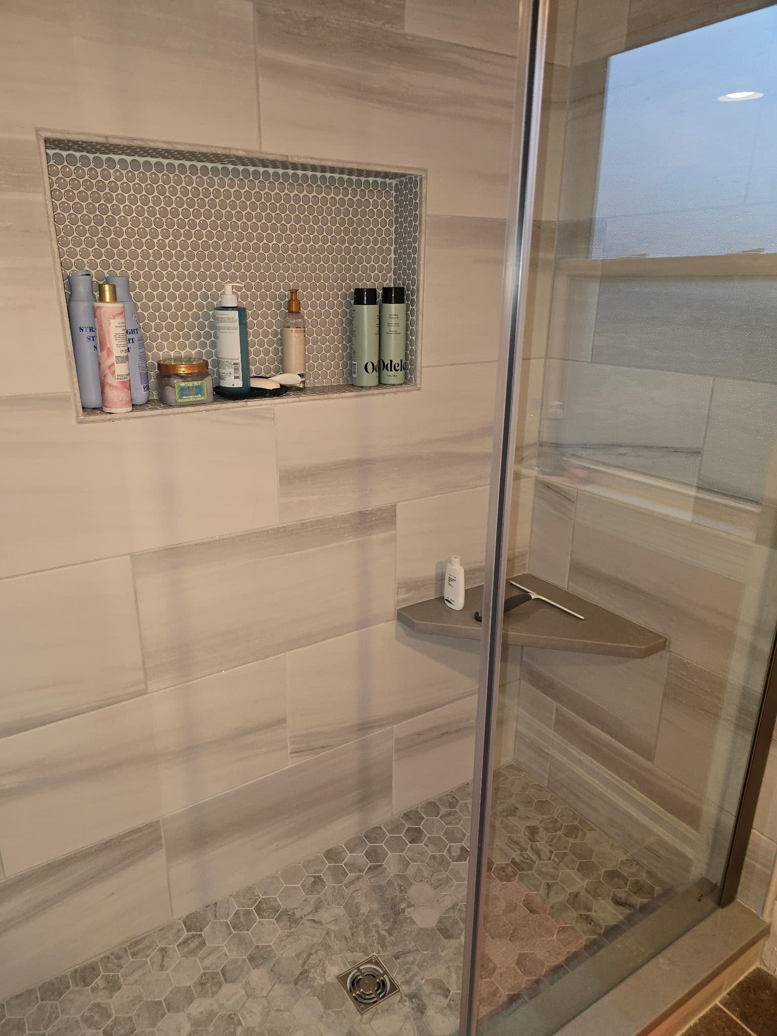 Walk-in shower with marble-look large-format tile, hex mosaic floor, and tile niche