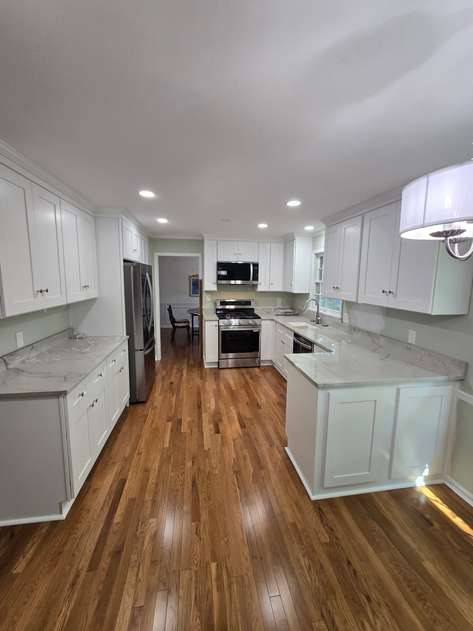 U-shaped white shaker kitchen with marble-look quartz countertops and hardwood floors